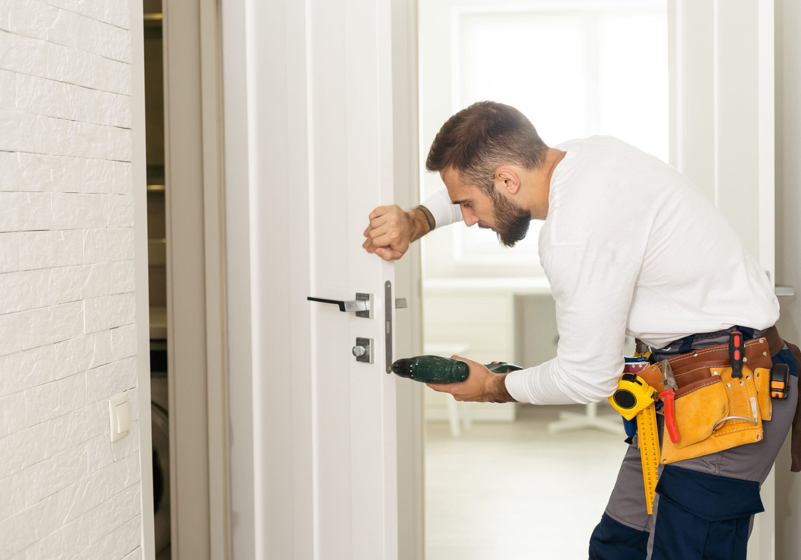 good looking man working as handyman and fixing a door lock in a house entrance.