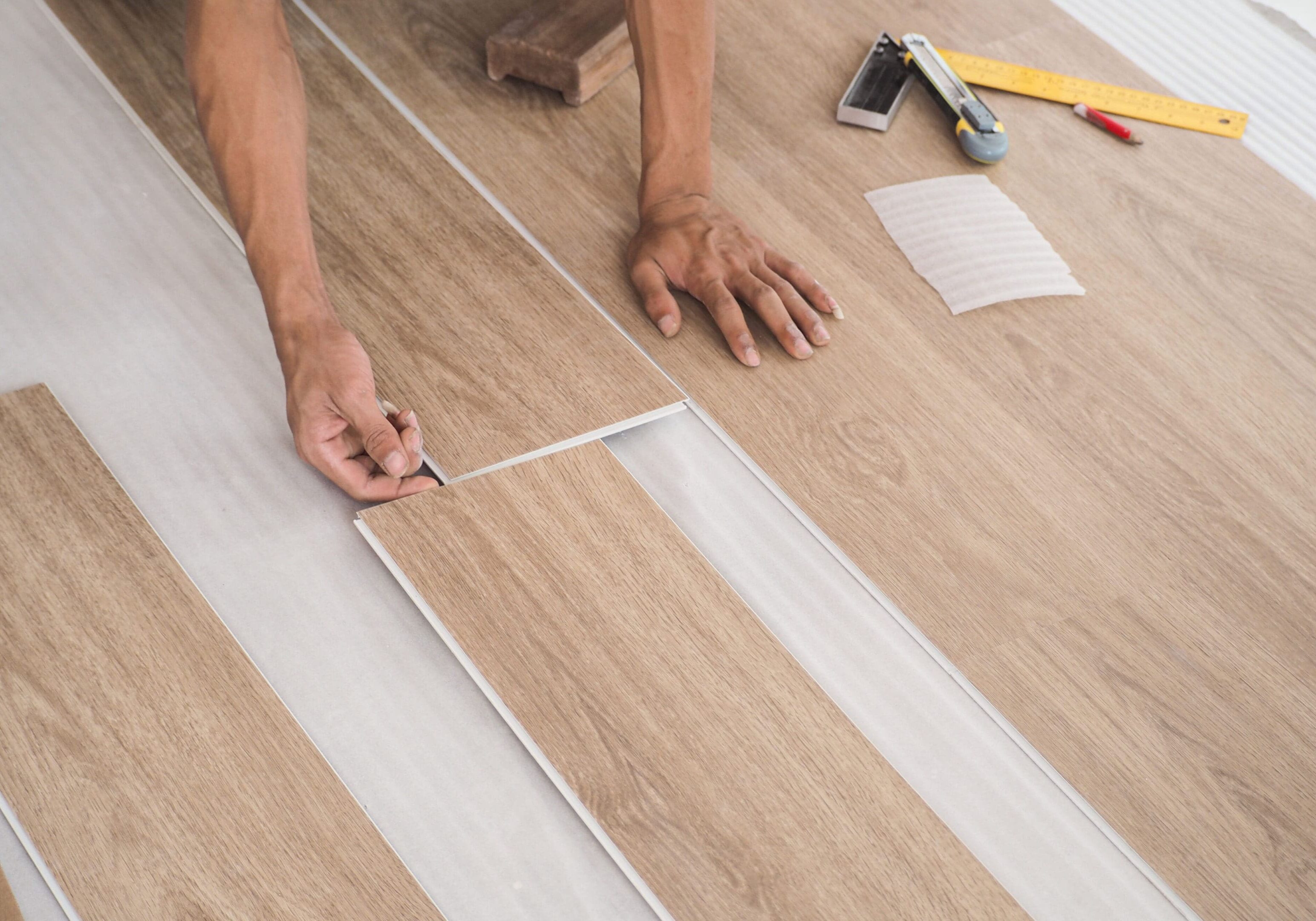 A technician is cutting luxury vinyl floor tiles with a cutter to lay the floor before placing it on the leveling foam.