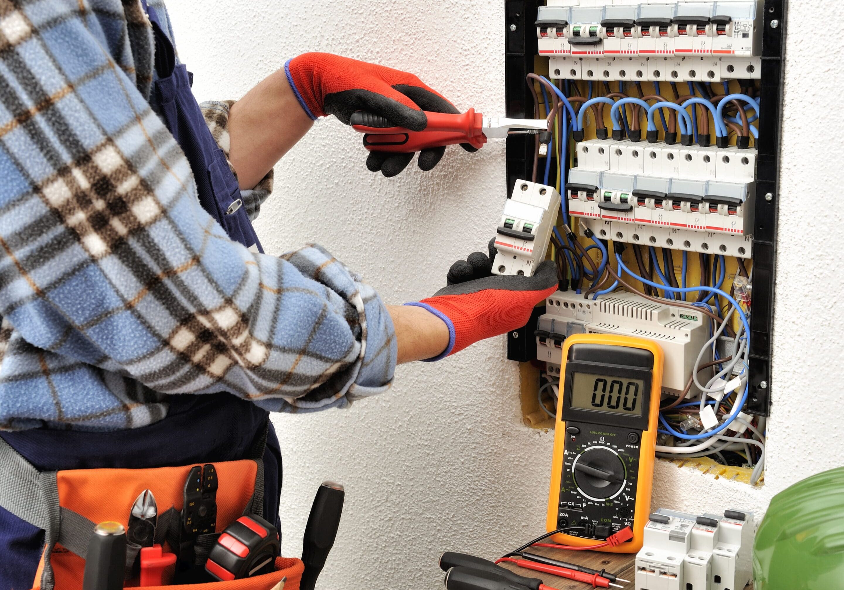 Young electrician technician introduces the electric cable into the clamp of the magnetothermic switch with an insulated clamp